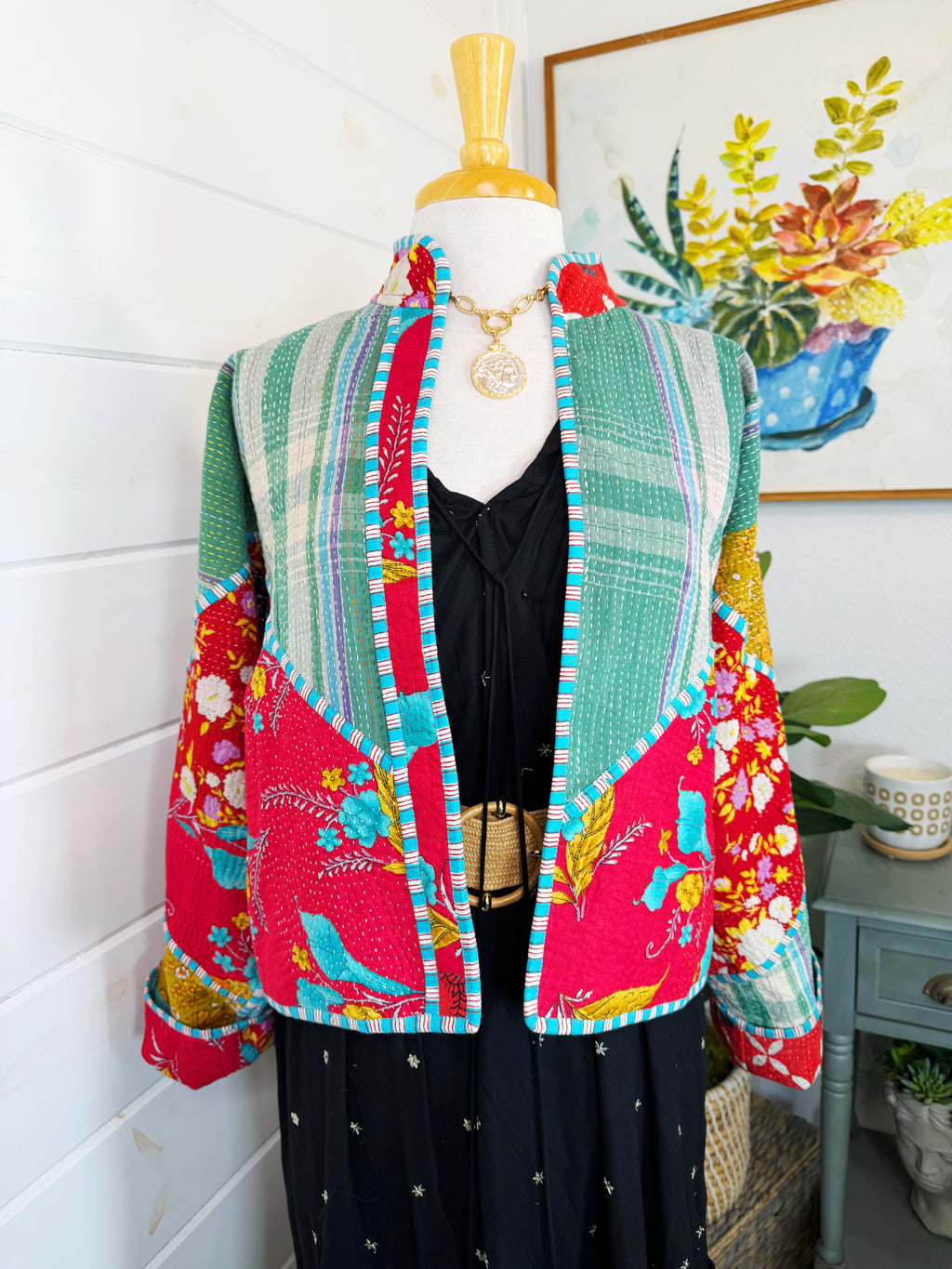 Colorful quilted jacket on a mannequin against a white wall with a plant in the background