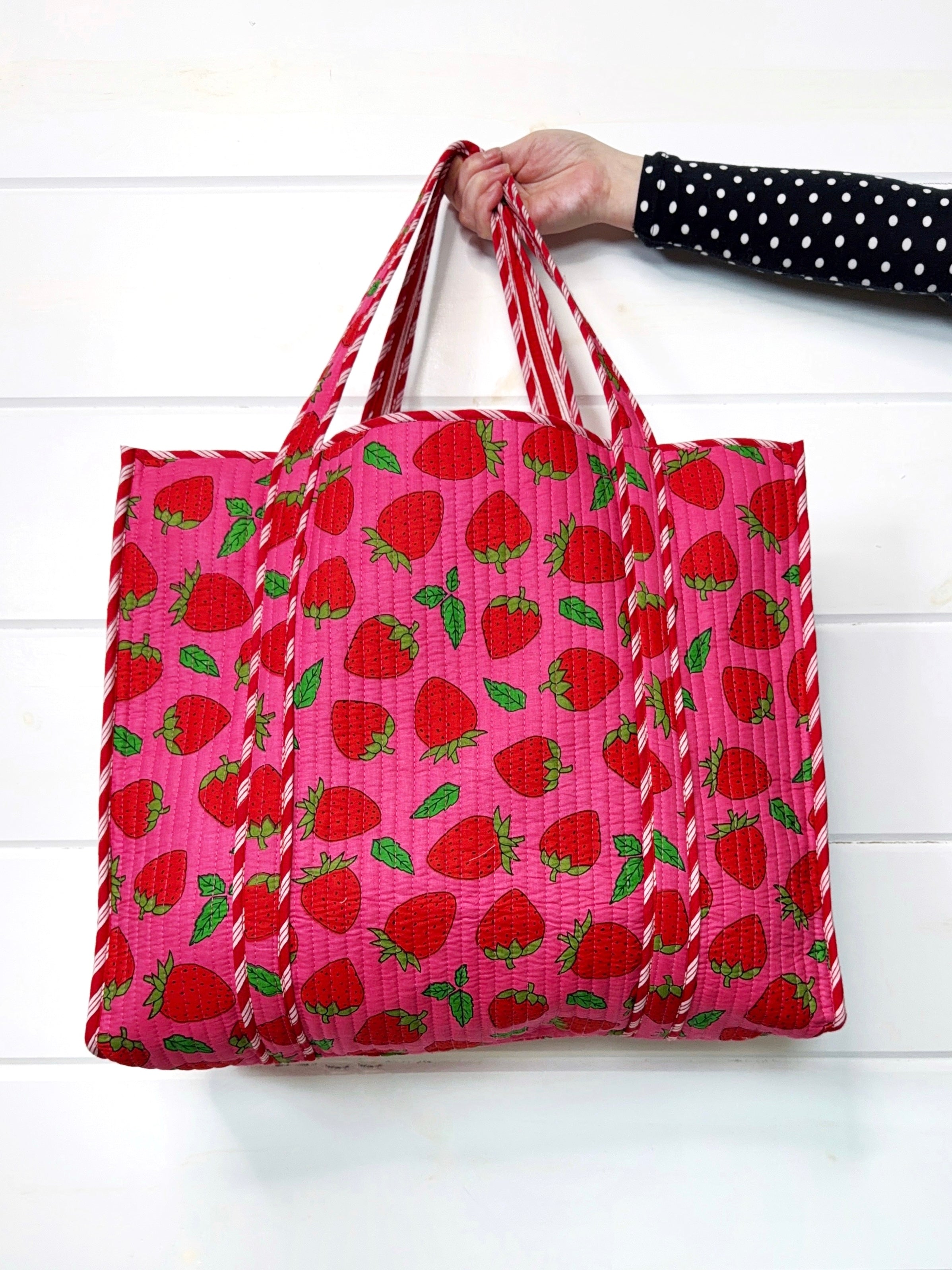 Pink strawberry tote bag by Folklore Couture with strawberry pattern held by a hand against a white background